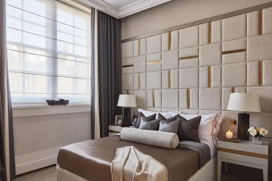 Upholstered panelled headboard wall in cream and brass in a Carlos Place bedroom, bespoke upholstery