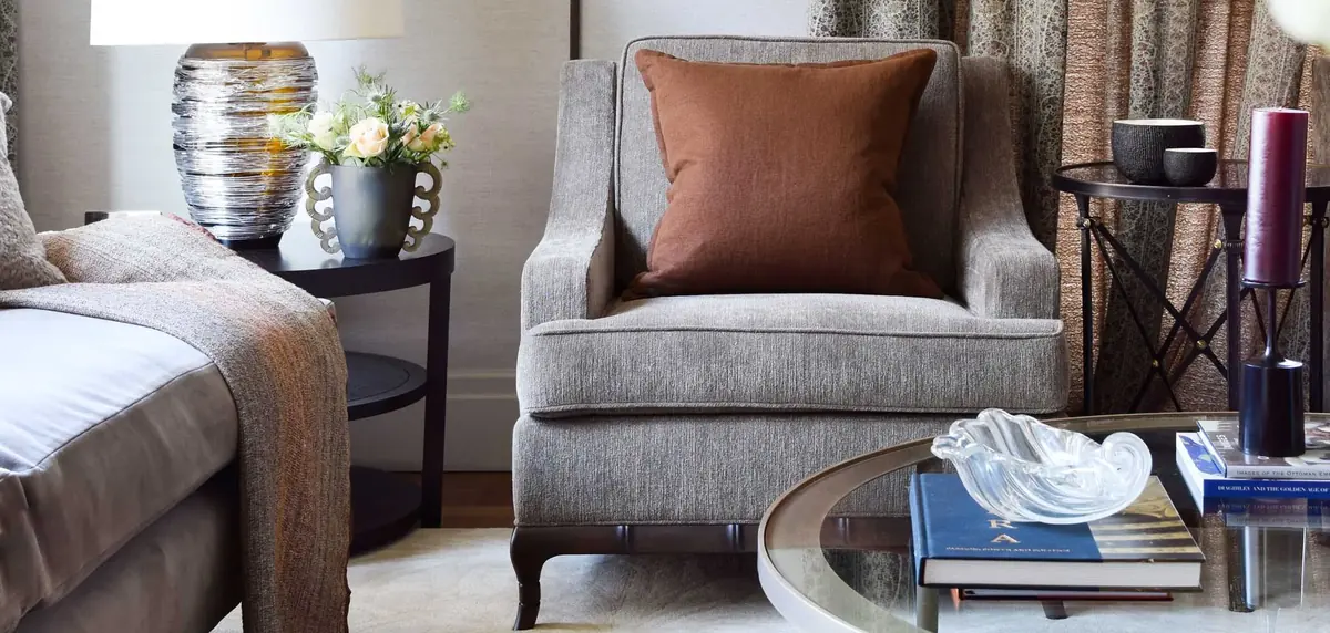 Taupe armchair with tan cushion beside a glass coffee table in an Ebury Square sitting room