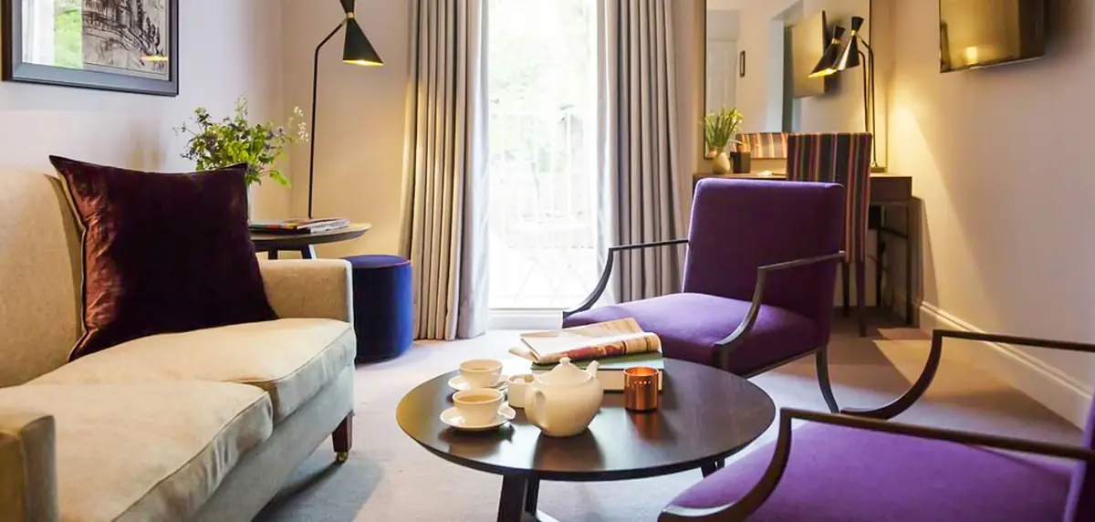 Hotel suite with purple velvet armchairs, round dark coffee table and cream sofa, Old Parsonage Hotel