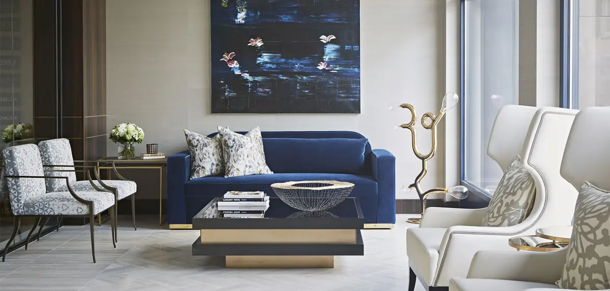 Blue velvet sofa, cream wing chairs and dark glass coffee table beneath a blue painting, Cheval Place