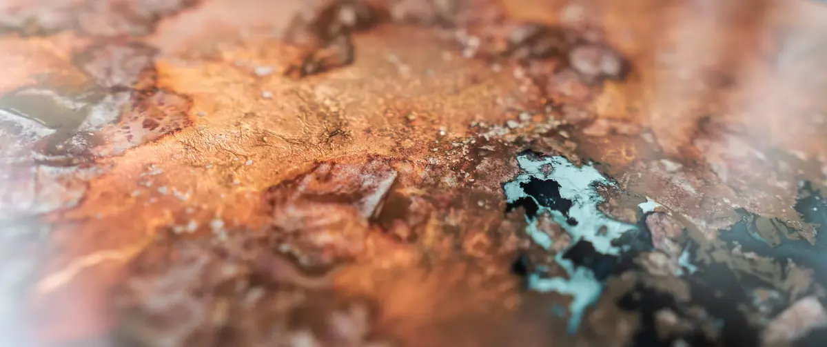 Macro detail of aged bronze leaf verre églomisé glass with orange and teal patina