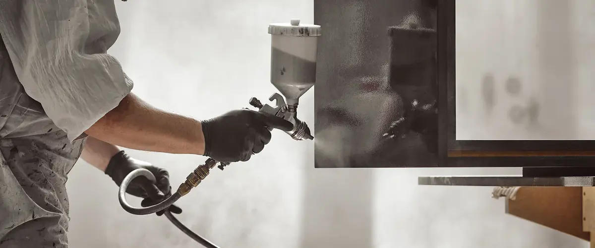 Craftsperson in black gloves hand spraying a lacquer finish onto a furniture panel