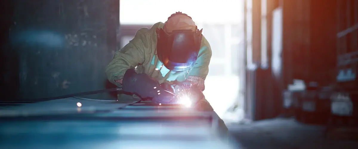 Welder with visor fusing steel under a bright arc, bespoke blackened steel metalwork