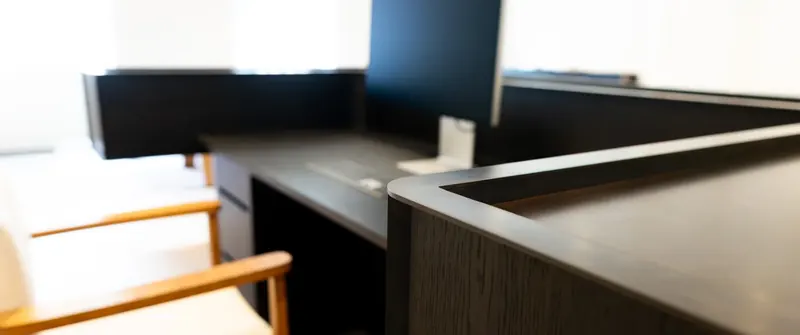 Dark timber office desk with monitor and pale chair in a bright room, bespoke office furniture