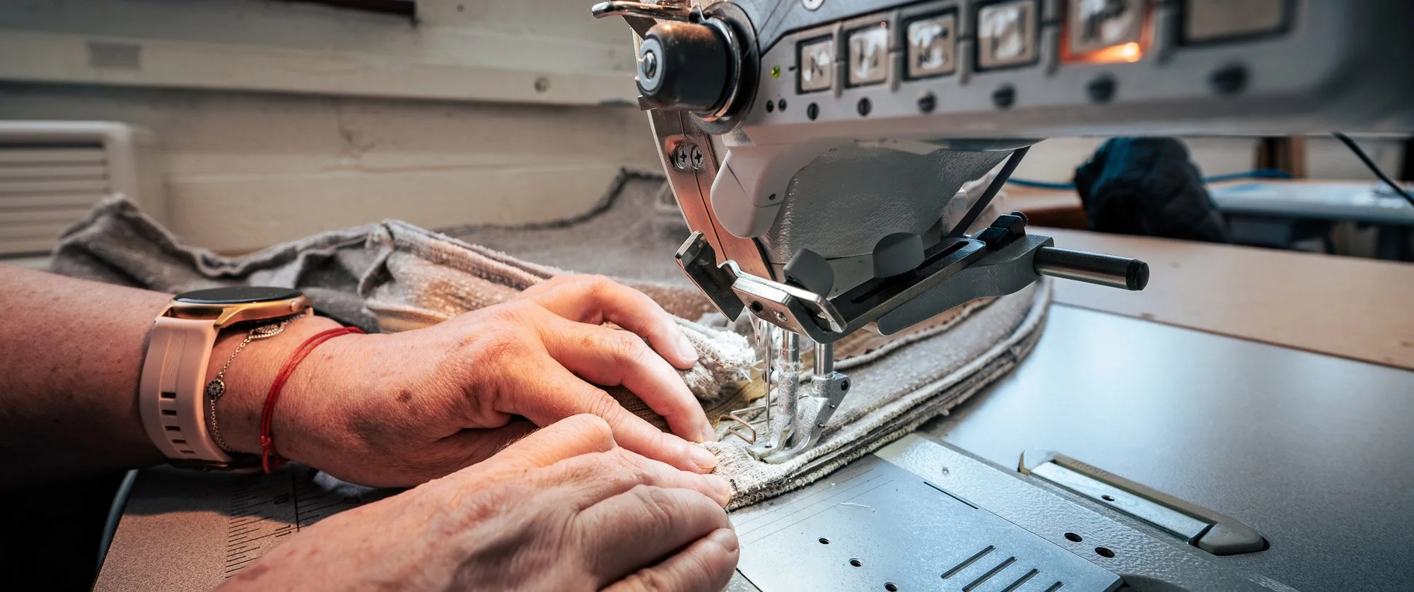 Hands feeding upholstery cloth through an industrial sewing machine, stitching a bespoke upholstered piece
