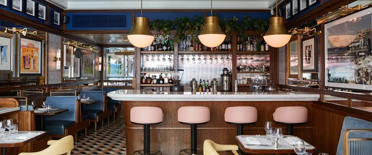 Café bar with white topped counter, pink stools, brass pendants and back shelving at Chucs, bespoke café joinery