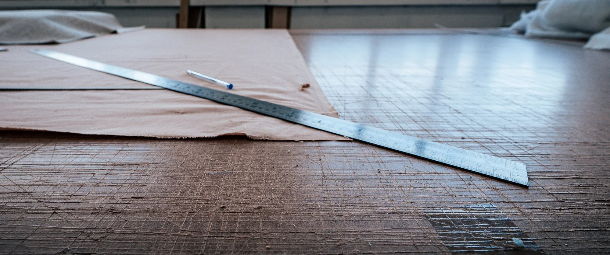 Steel rule laid across fabric on a timber cutting table in an upholstery workshop, measuring before cutting