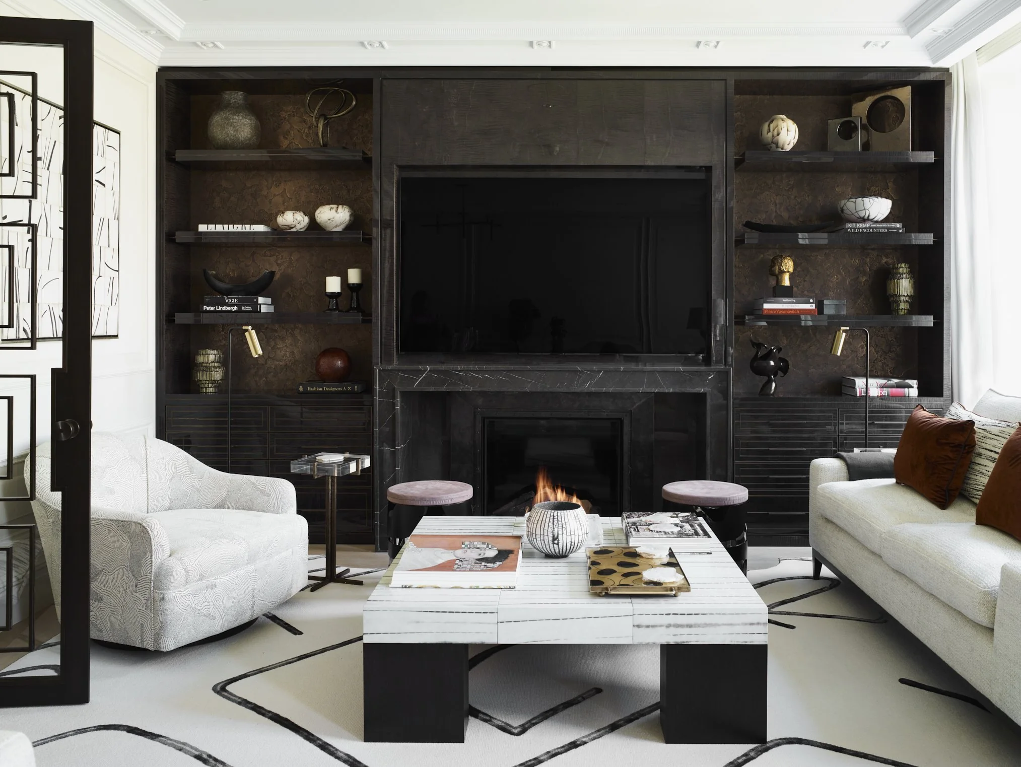 Black built in display cabinets with lit shelves of objects either side of a fireplace and screen
