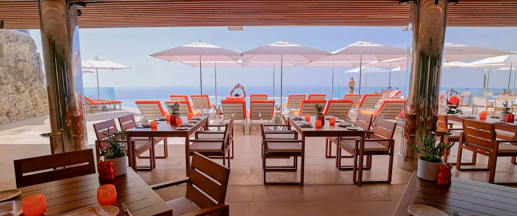 Timber outdoor dining tables and chairs on a covered sea terrace with loungers at Maybourne Riviera