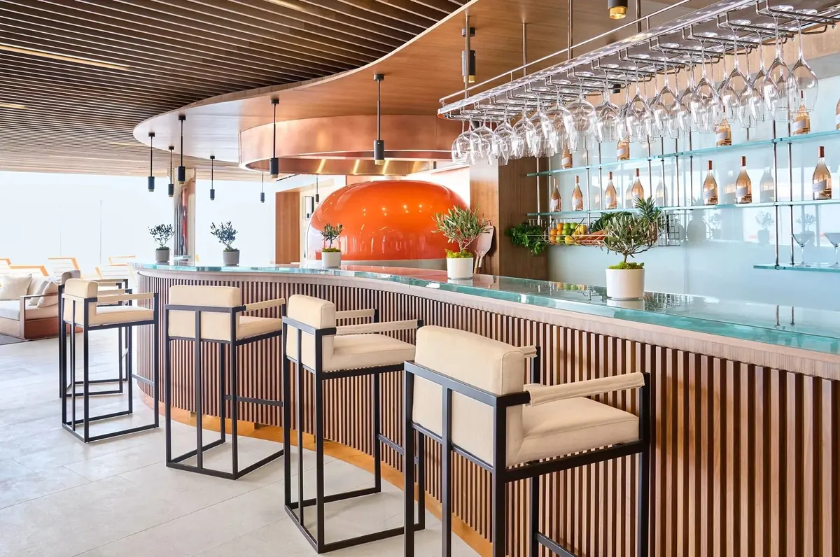 Curved fluted timber bar with high stools, hanging glass rack and slatted ceiling, Maybourne Riviera