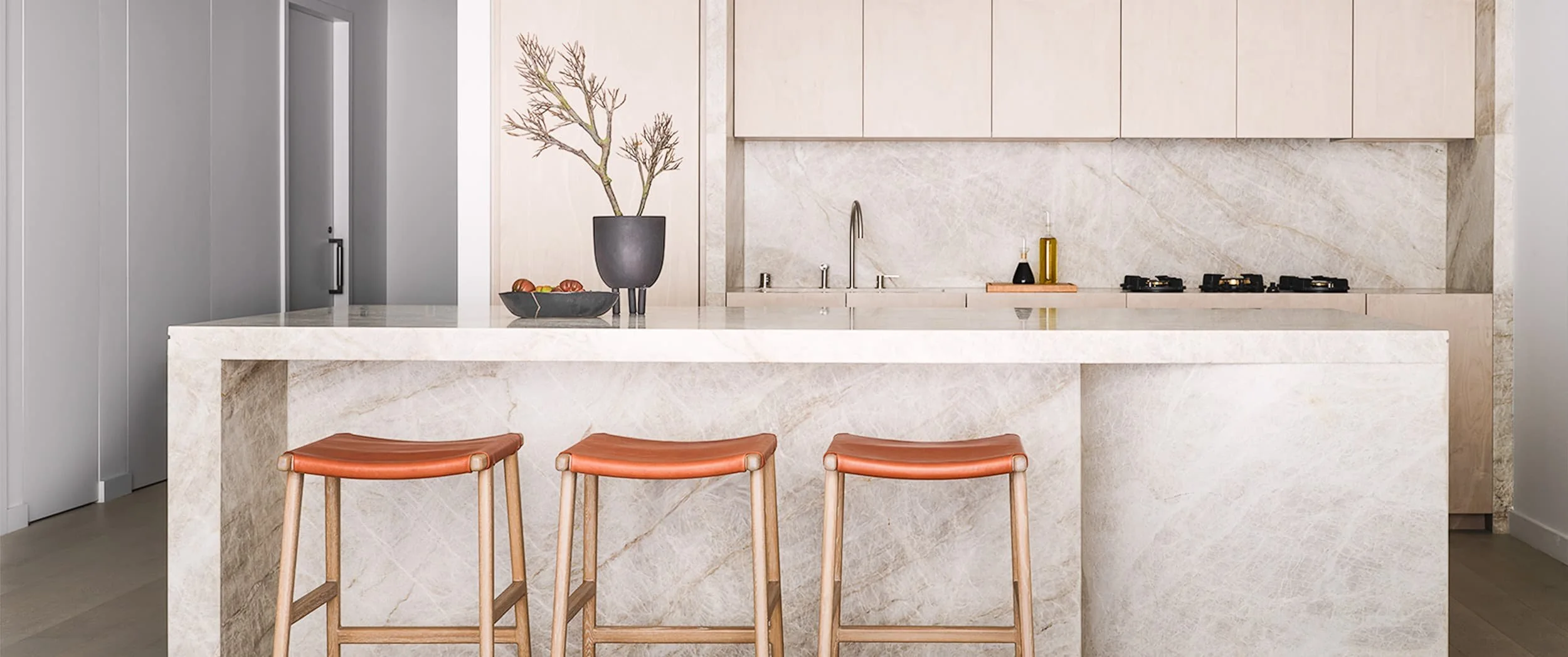 Veined quartzite waterfall edge kitchen island with three tan stools and white cabinetry behind