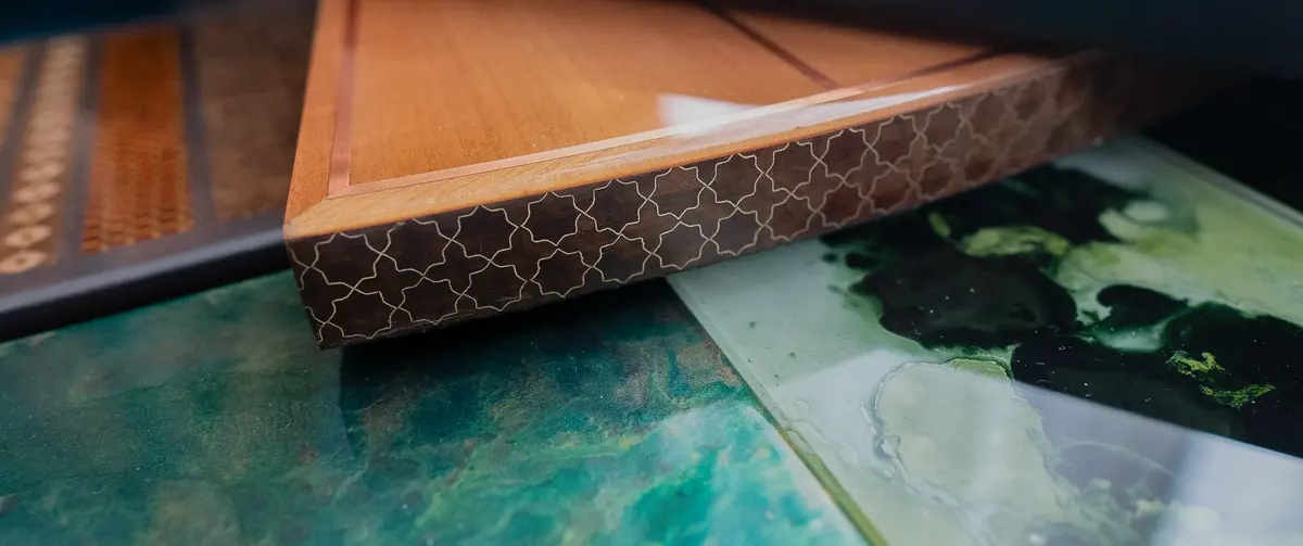 Timber panel edged with fine geometric inlay resting on teal lacquer samples, bespoke material palette