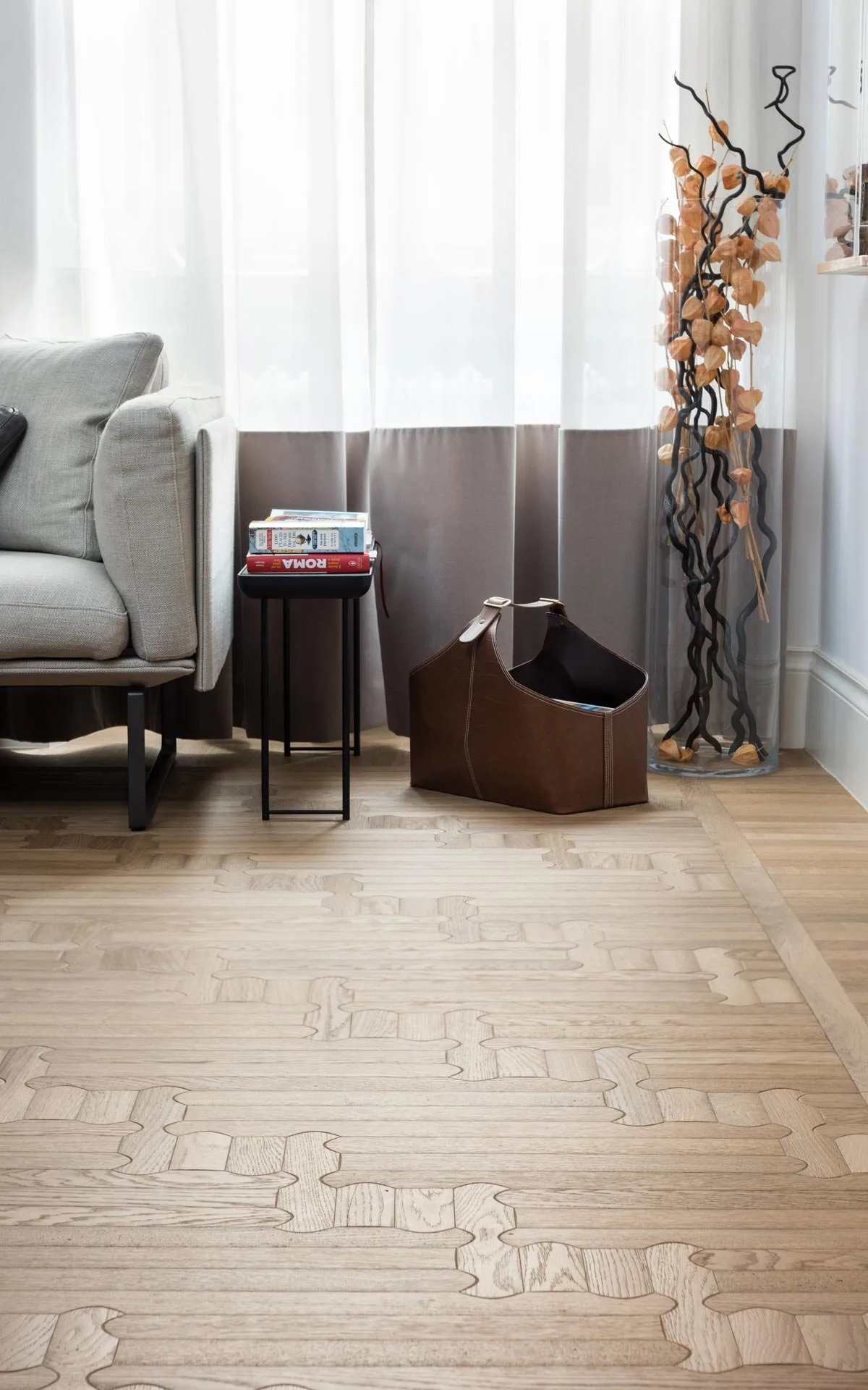 Biscuit oak floor in a living room corner with a grey armchair and sheer curtains, laid with interlocking rounded boards