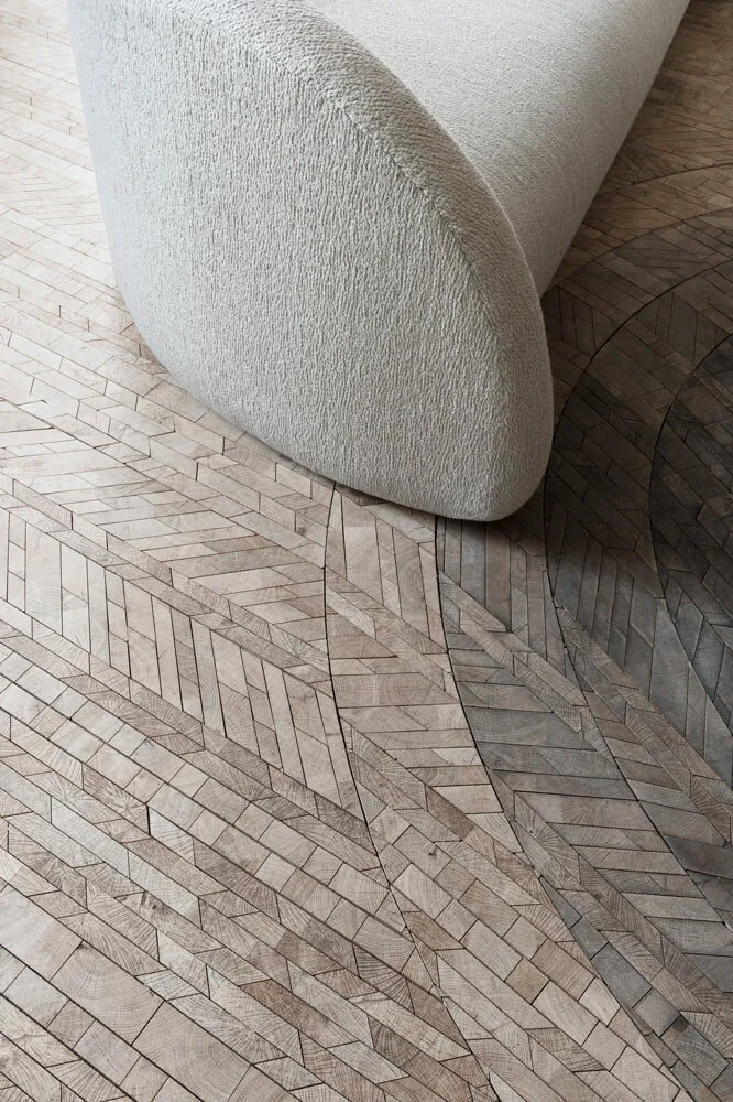 Forêt end-grain oak floor with curved herringbone bands running around a pale upholstered stool