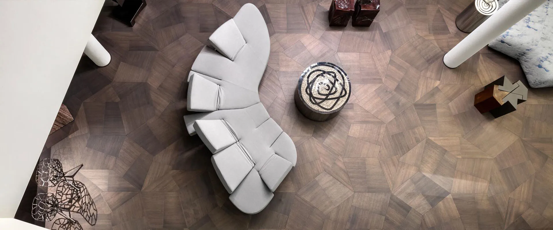 Slide dark oak modules laid as an angular geometric floor around a curved white sofa, seen from above