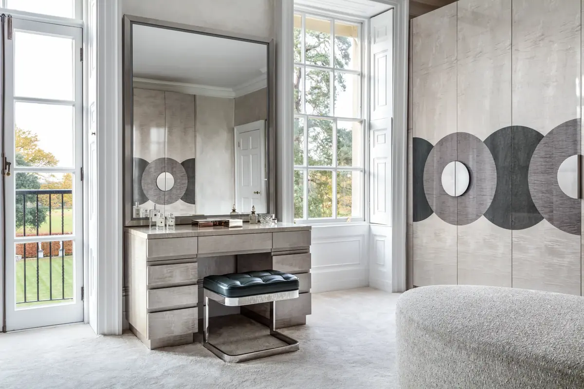 Dressing table with leather stool beside wardrobe doors with circular graphic panels, bespoke dressing room joinery