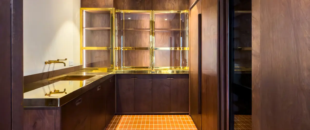 Completed utility room at Camberwell House with polished brass worktop and sink, curved glazed brass doors, tiles.