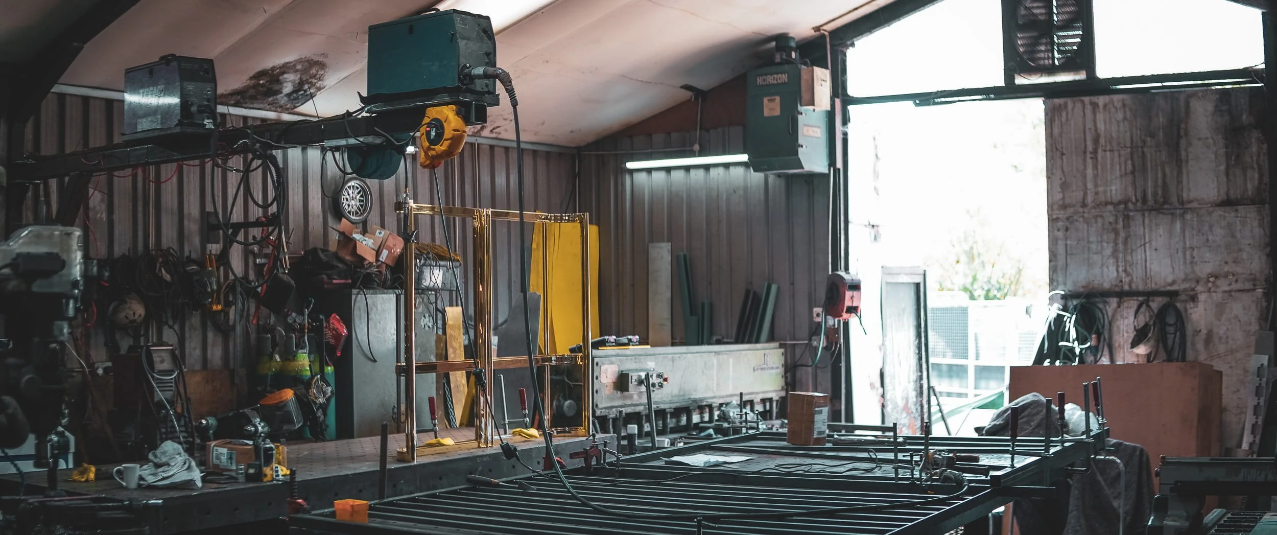 Metal workshop bay at Make Bespoke Studio with welding equipment, extraction units and a polished brass door frame standing on the fabrication bench.