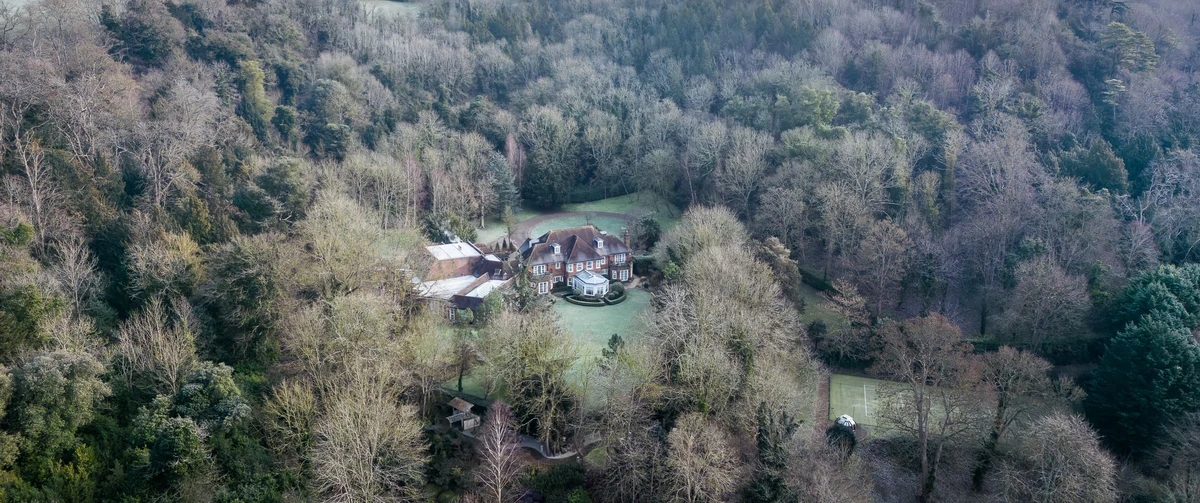 Aerial view of a brick country house set in a clearing surrounded by winter woodland in rural Oxfordshire, the setting for the Country Home Cinema project by Make Bespoke Studio.