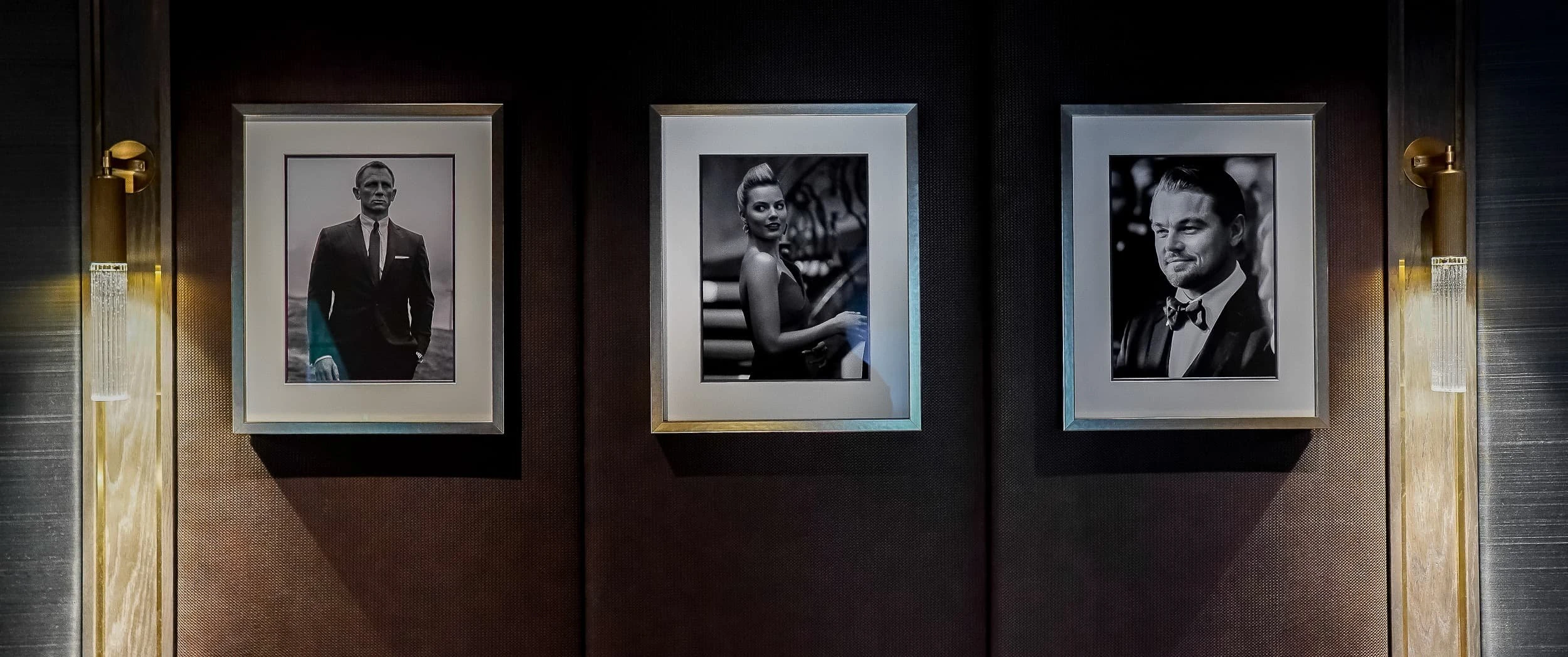 Three framed black-and-white portraits of film actors hung on a leather-clad wall between brass and glass wall lights in the Country Home Cinema.