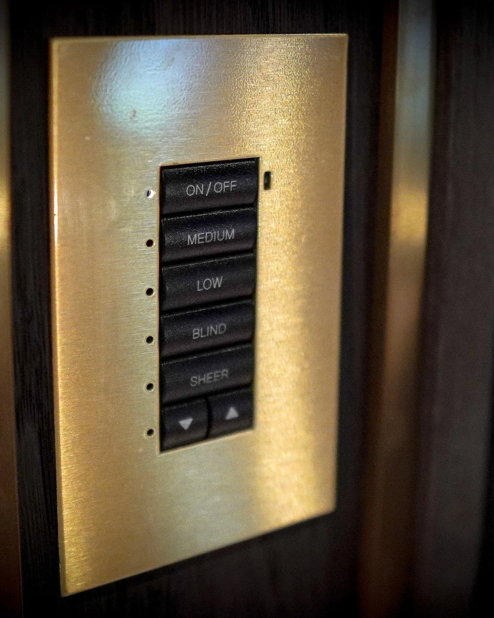 Angled close view of the engraved brass lighting keypad recessed into grey oak panelling in the Country Home Cinema.