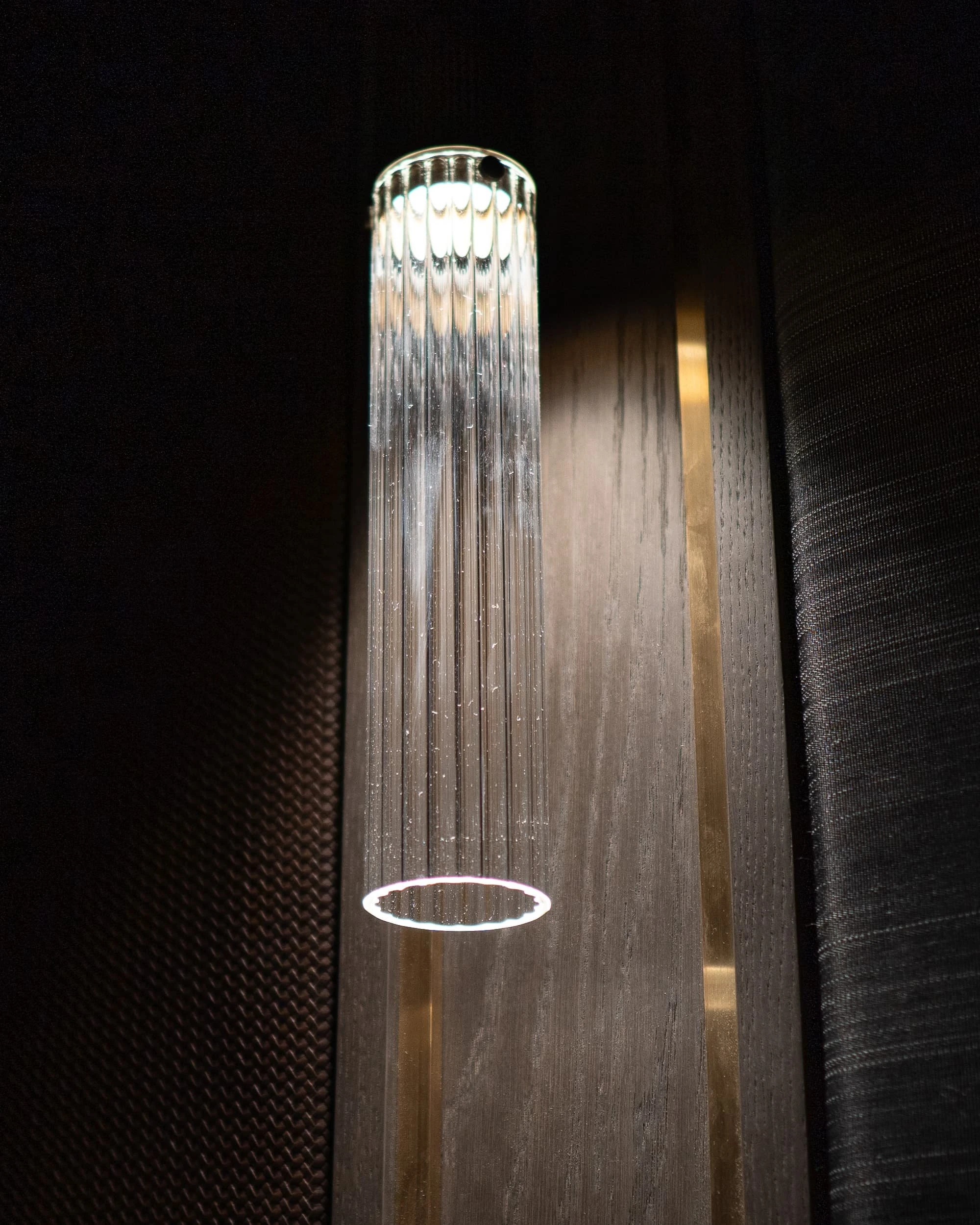 Vertical fluted glass wall light lit against a grey oak upright inlaid with brass, flanked by woven leather and textured wall fabric in the Country Home Cinema.