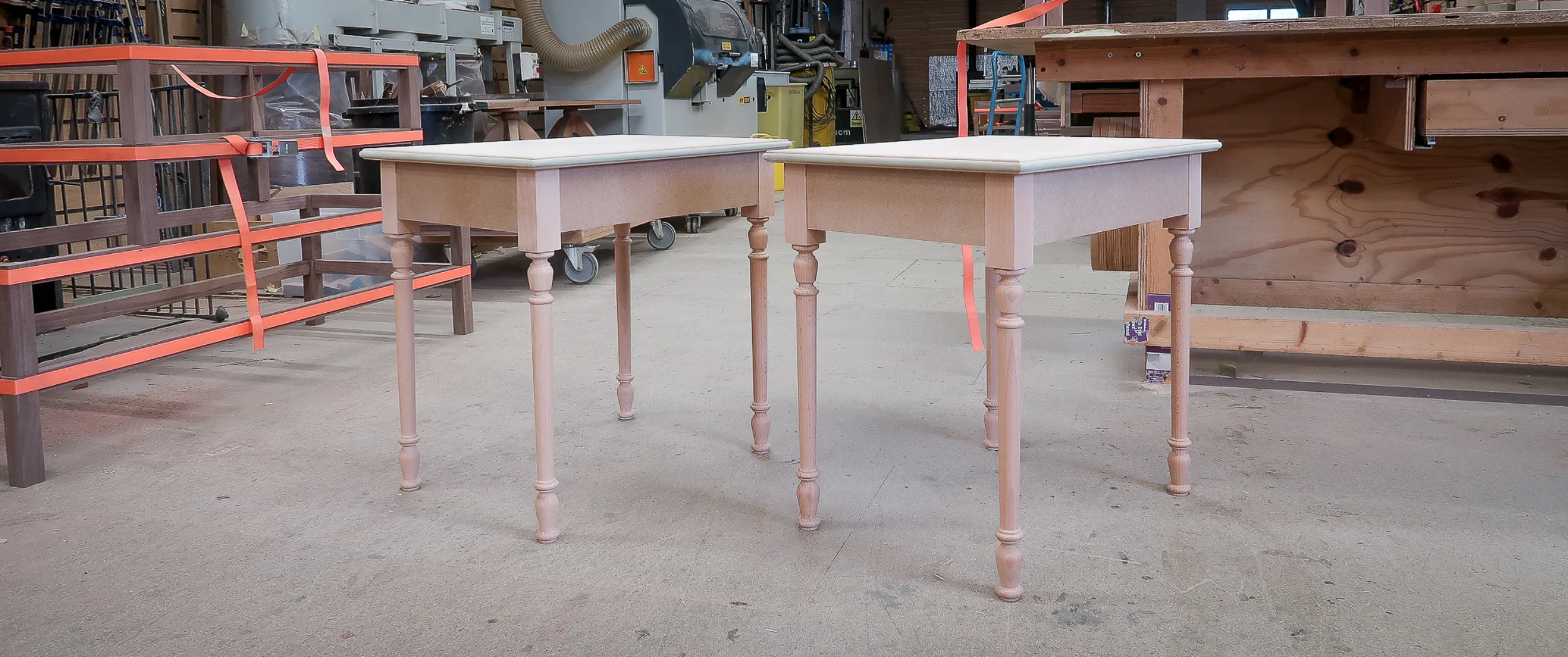 A matched pair of side tables with turned legs, in bare timber before finishing, in the workshop.
