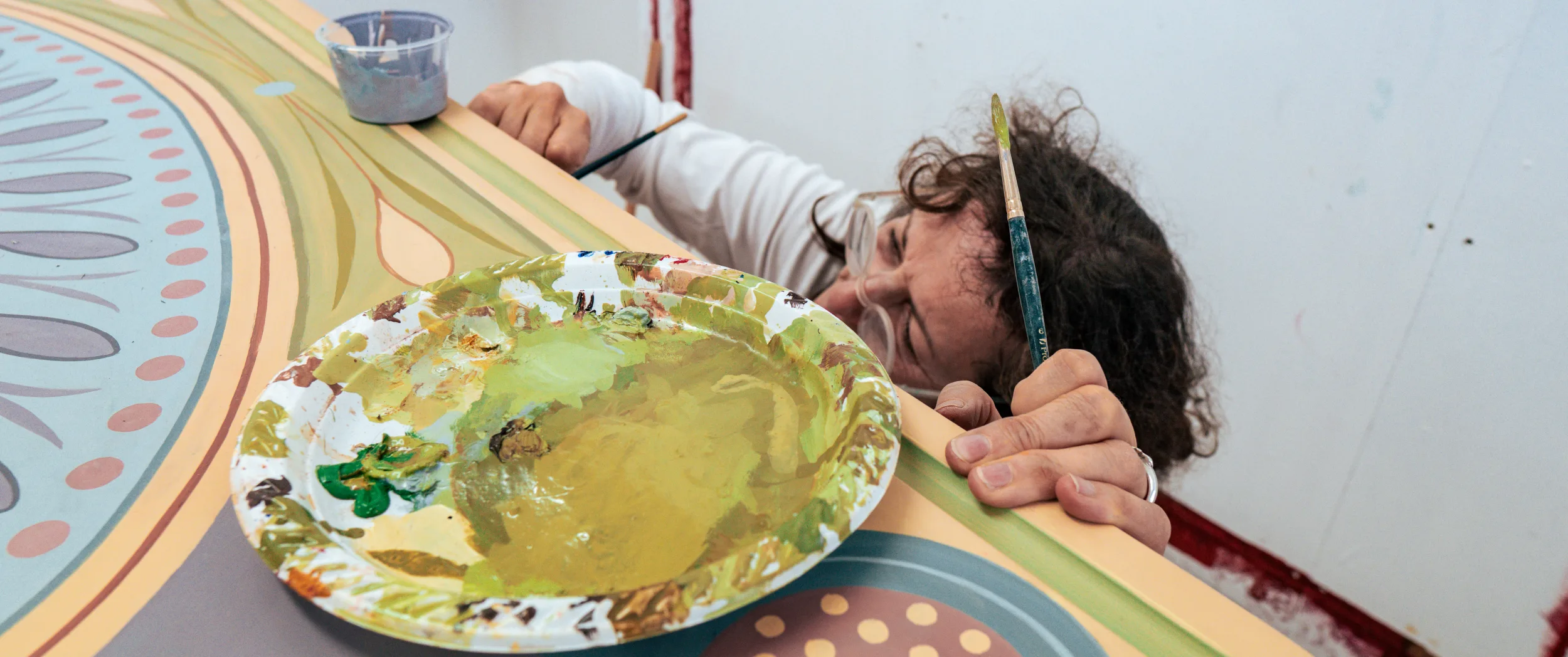 Lizzi Porter leaning over a tabletop, palette in hand, painting the central medallion.