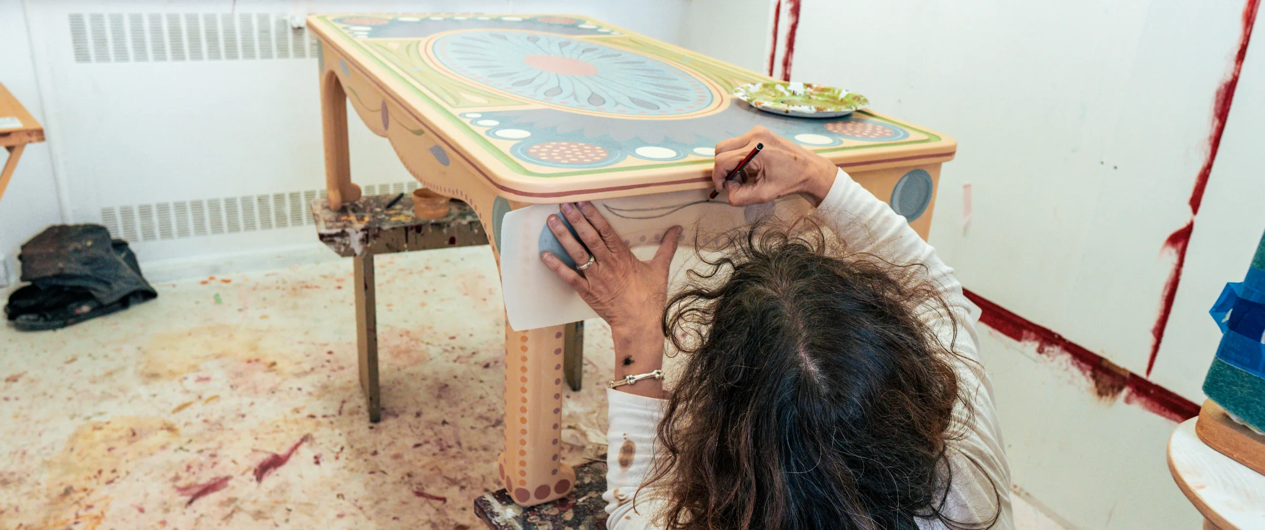 The artist reaching across a table, working paint into the design.