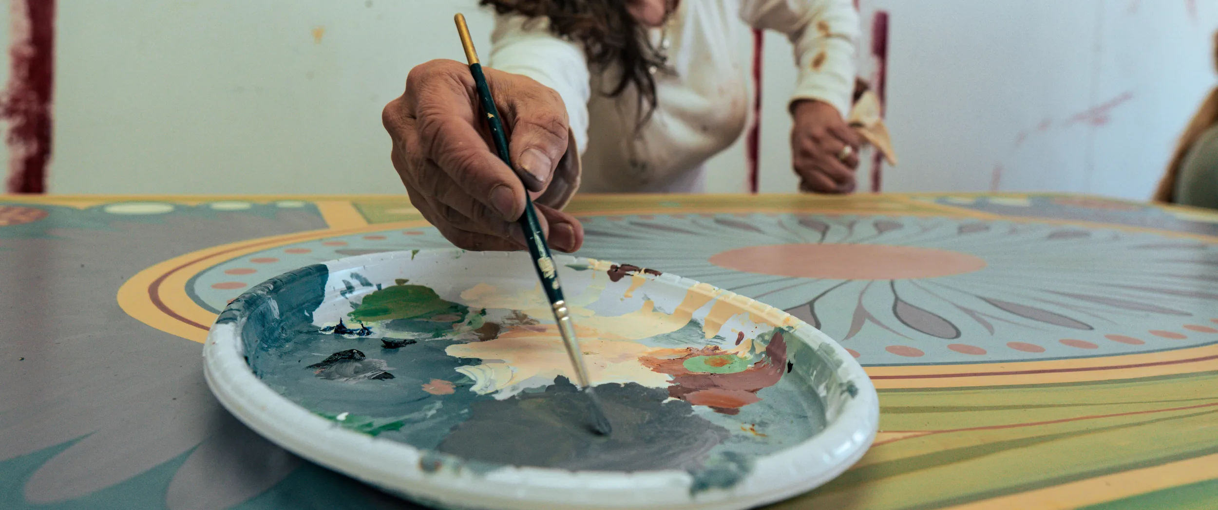 A brush mixing a colour on the oval palette resting on the painted top.