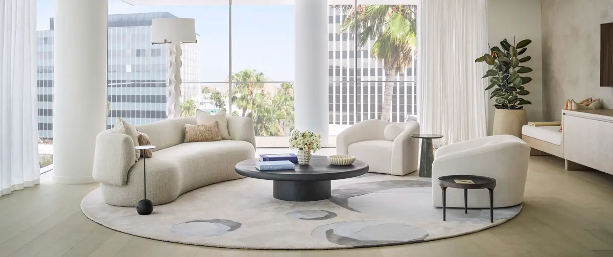 Residential living room with curved cream sofa, round coffee table and armchairs by tall windows, bespoke furniture