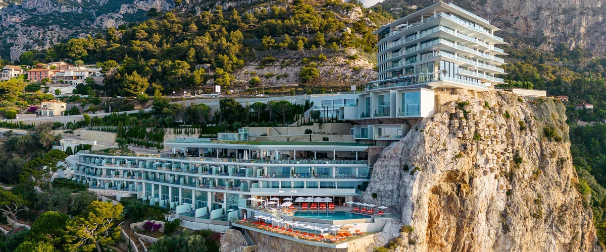 Aerial view of The Maybourne Riviera at Roquebrune-Cap-Martin, its white terraced floors and pool deck stepping down a limestone cliff above the Côte d'Azur.