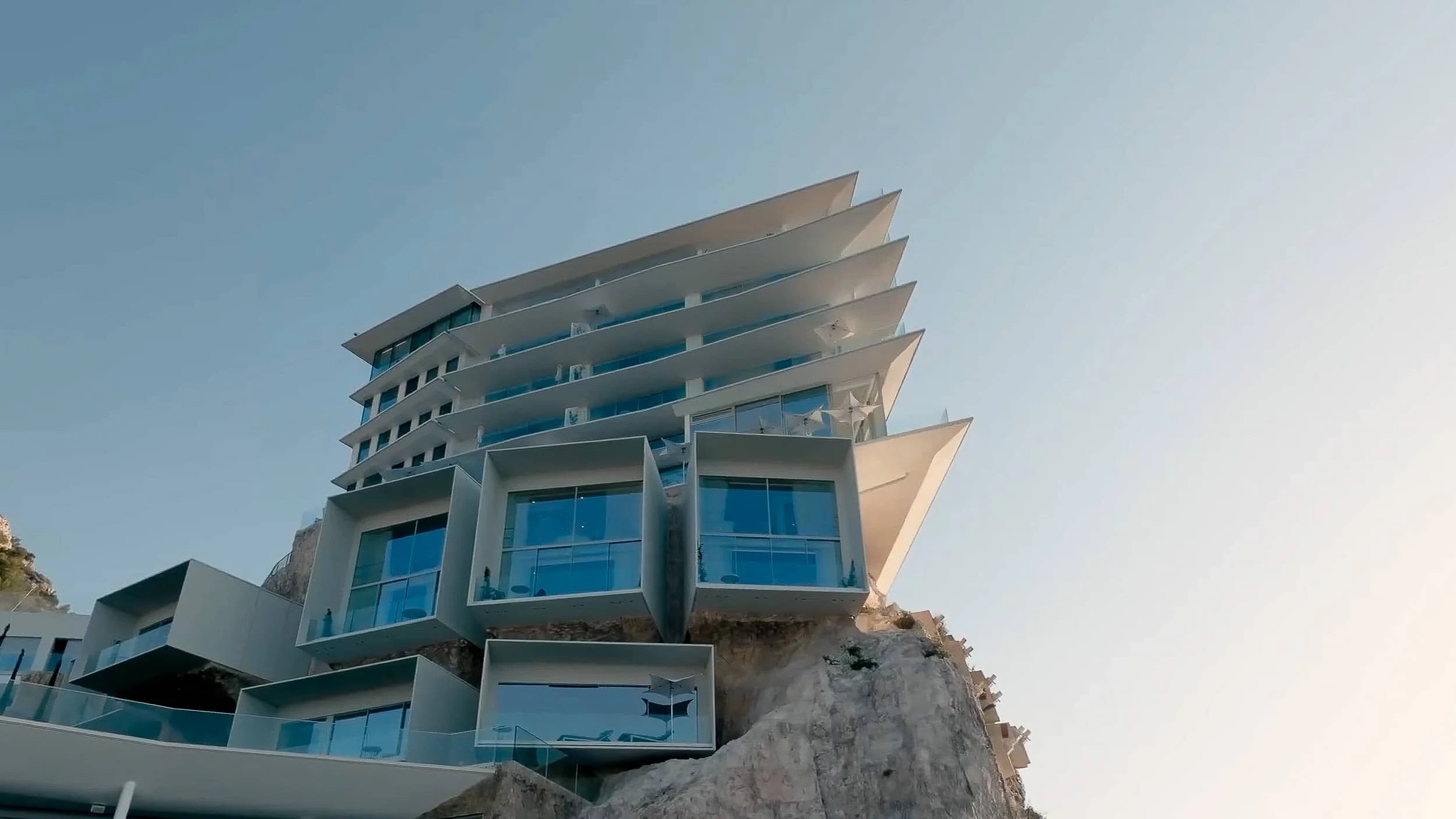 Upward view of the hotel's projecting white floor slabs and the angular glazed suite volumes cantilevered from the cliff at Roquebrune-Cap-Martin.