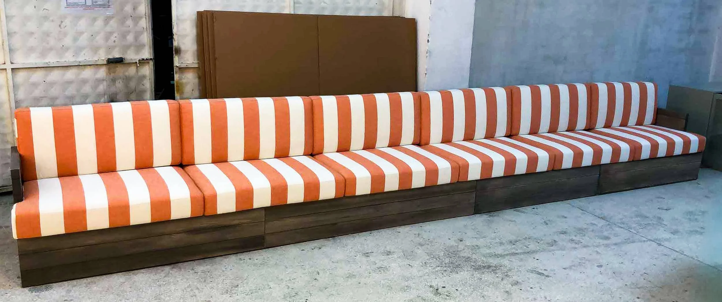 Long timber-based banquette with orange-and-white striped cushions photographed in the workshop before delivery to The Maybourne Riviera.