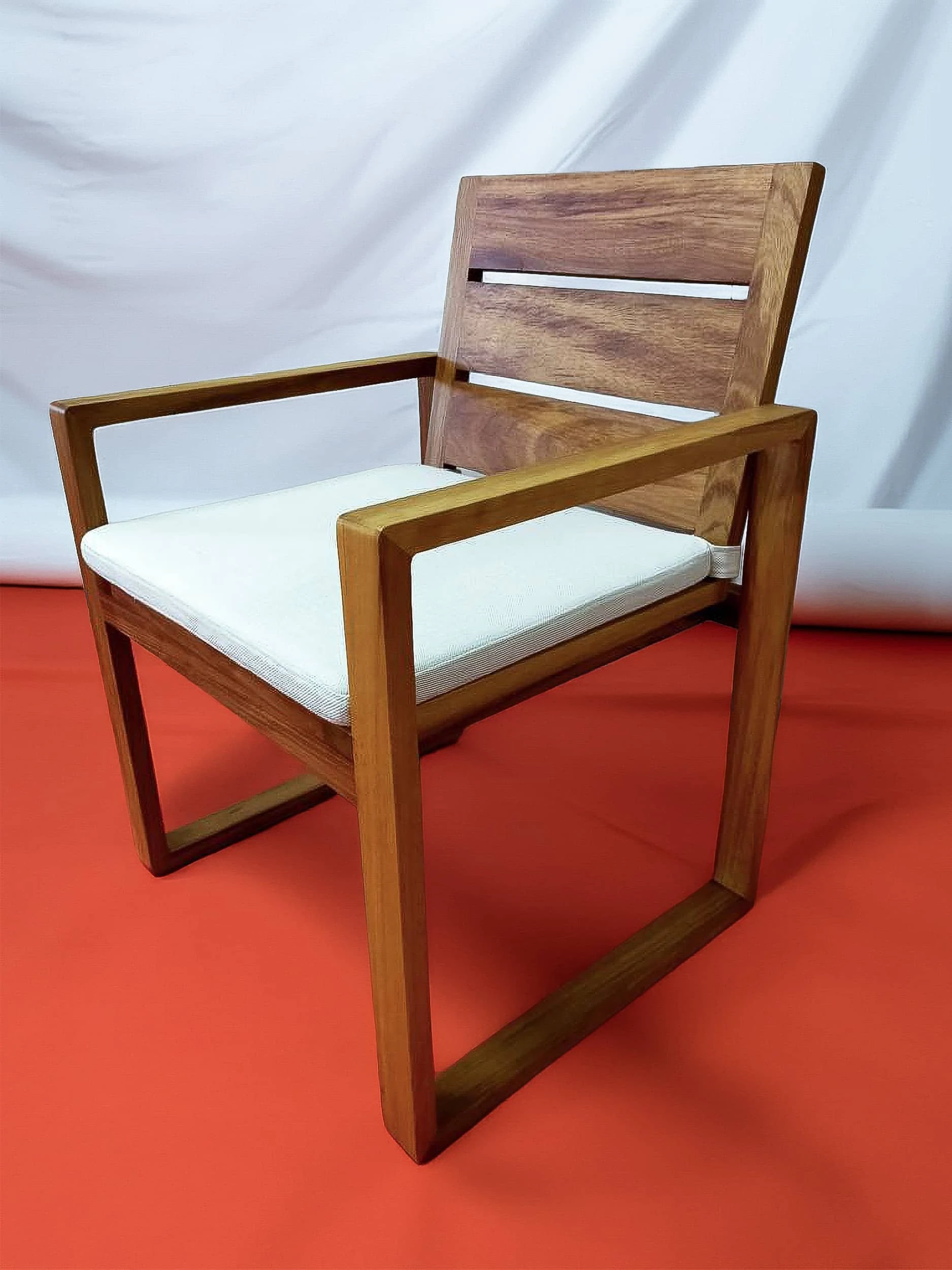 Iroko armchair with a slatted back, open frame arms and a white seat cushion photographed against a plain backdrop.