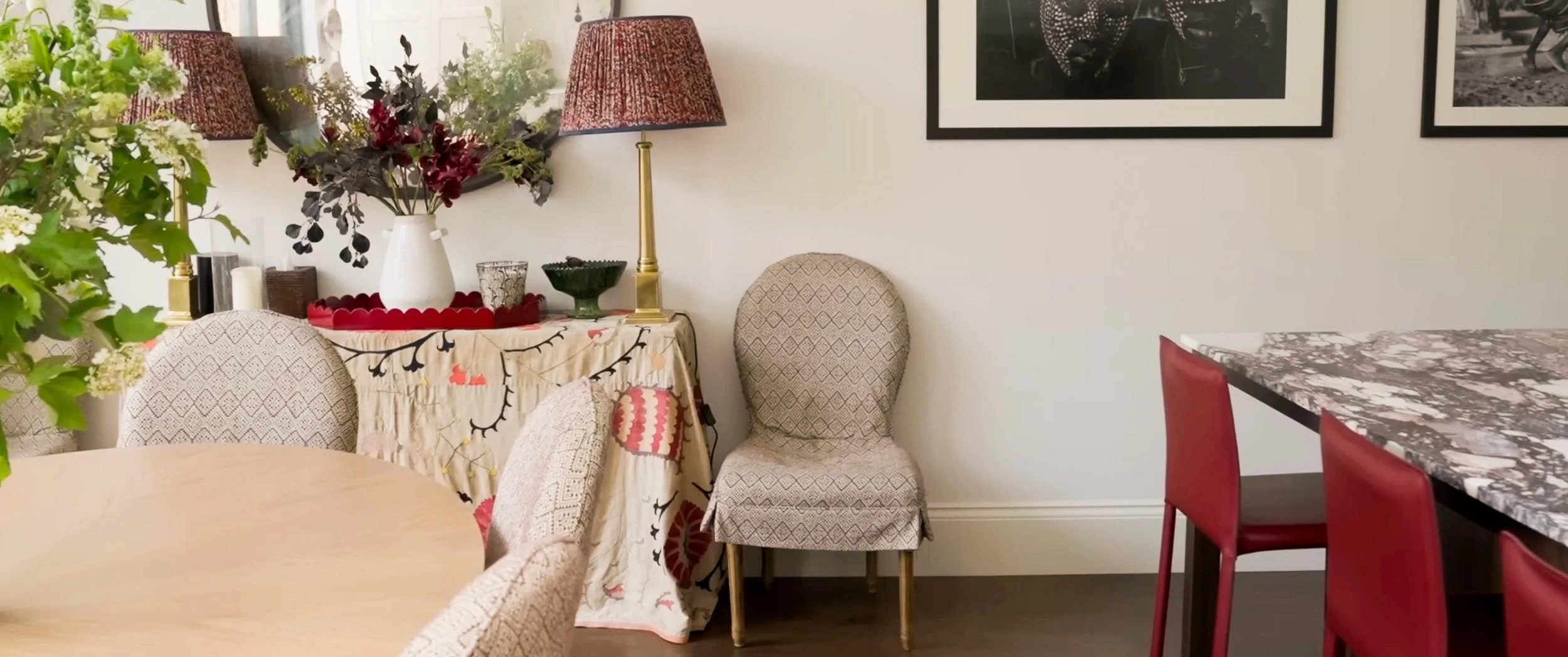 Dining corner in the Notting Hill house with a skirted console table, brass lamp, framed photographs and slipcovered chairs beside a marble-topped counter.
