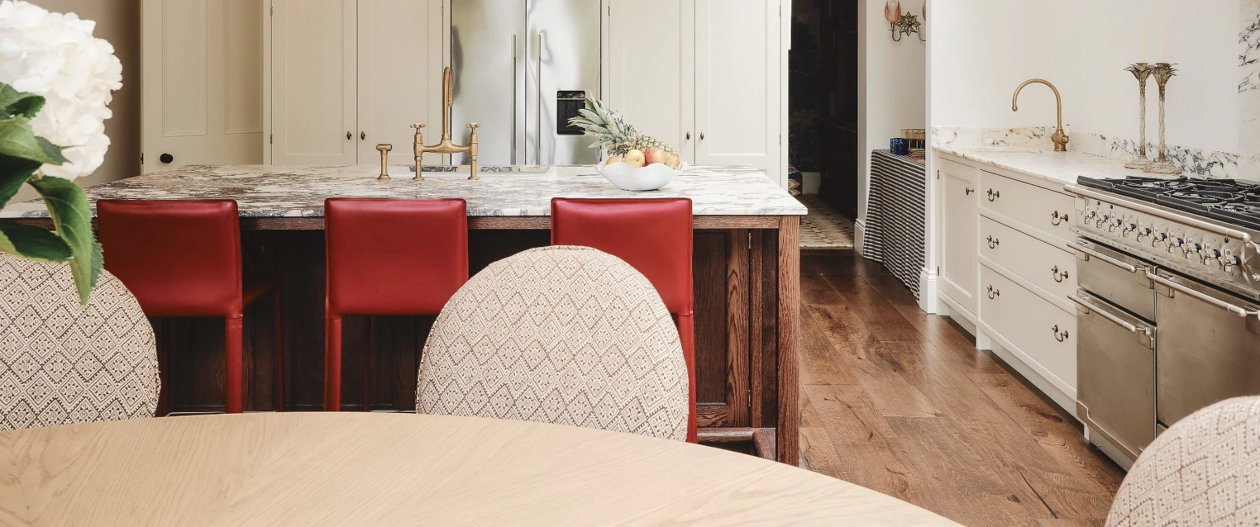 Red leather stools at the marble-topped oak island in the Notting Hill kitchen, with the oak dining table in the foreground and the range beyond.