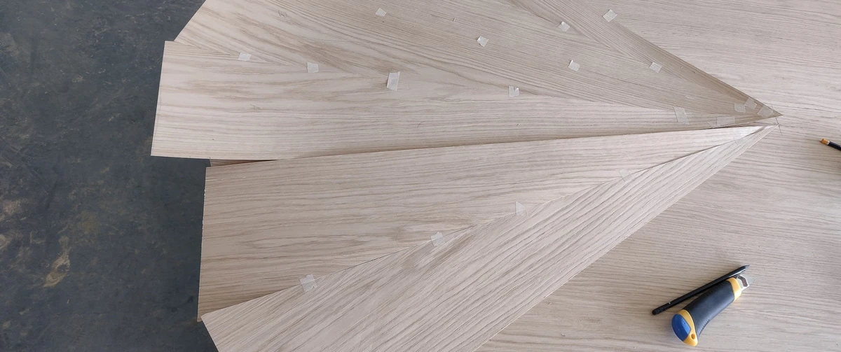 Oak veneer leaves cut and taped in mirrored pairs on the workshop bench for a starburst table top
