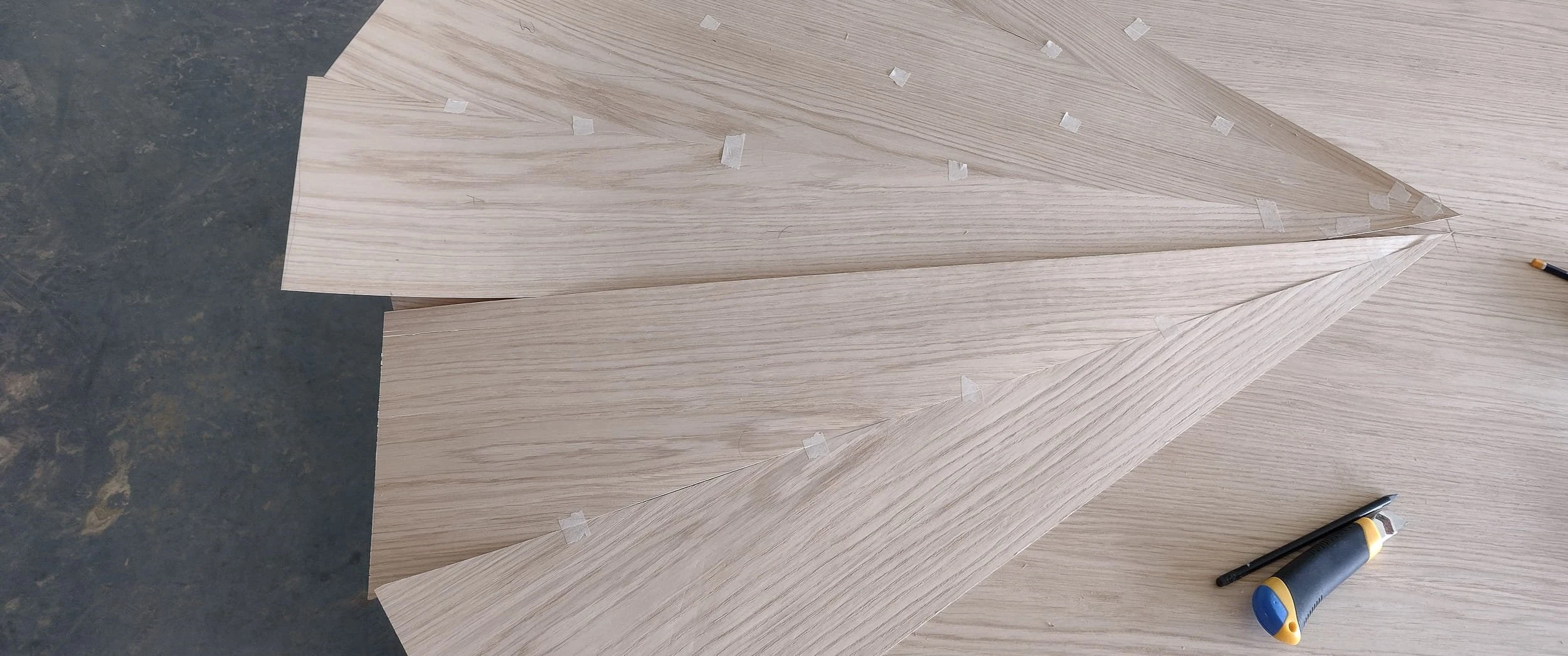 Oak veneer leaves cut and taped in mirrored pairs on the workshop bench, part of the starburst lay-up for the Notting Hill dining table top.