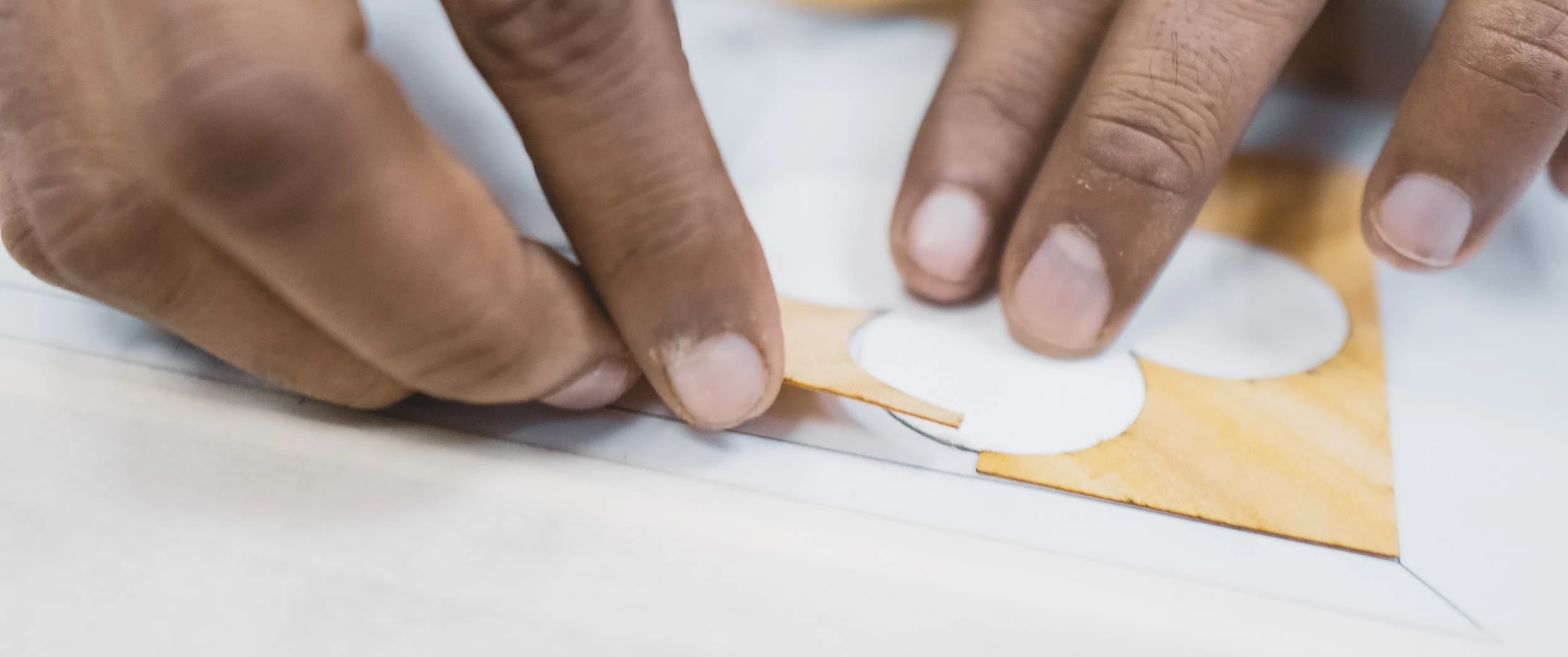 Two hands pressing a white mother of pearl quatrefoil into its recess in a pale veneer field, part of the hand assembly for the Rowes Wharf Apartment panels.