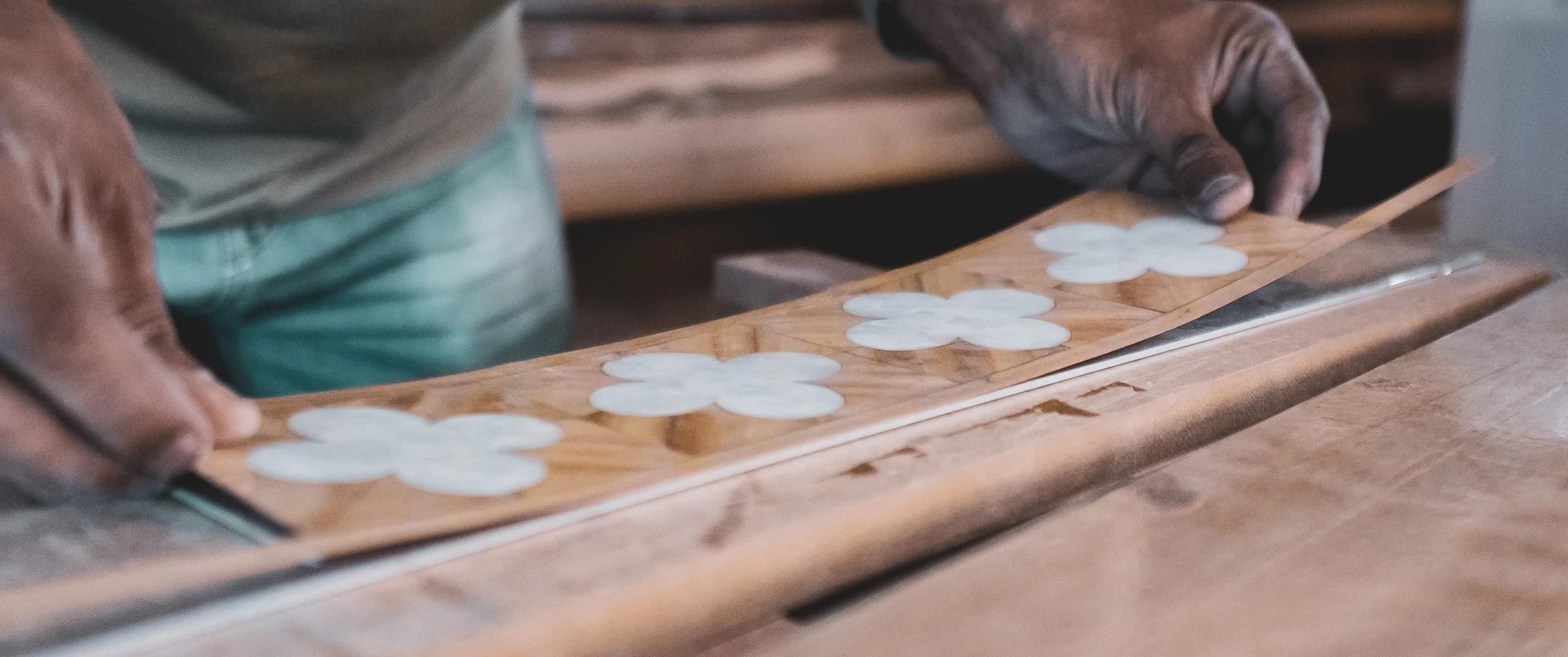 A maker lifting a flexible assembled veneer border set with mother of pearl quatrefoils across the workbench, part of the Rowes Wharf Apartment marquetry.