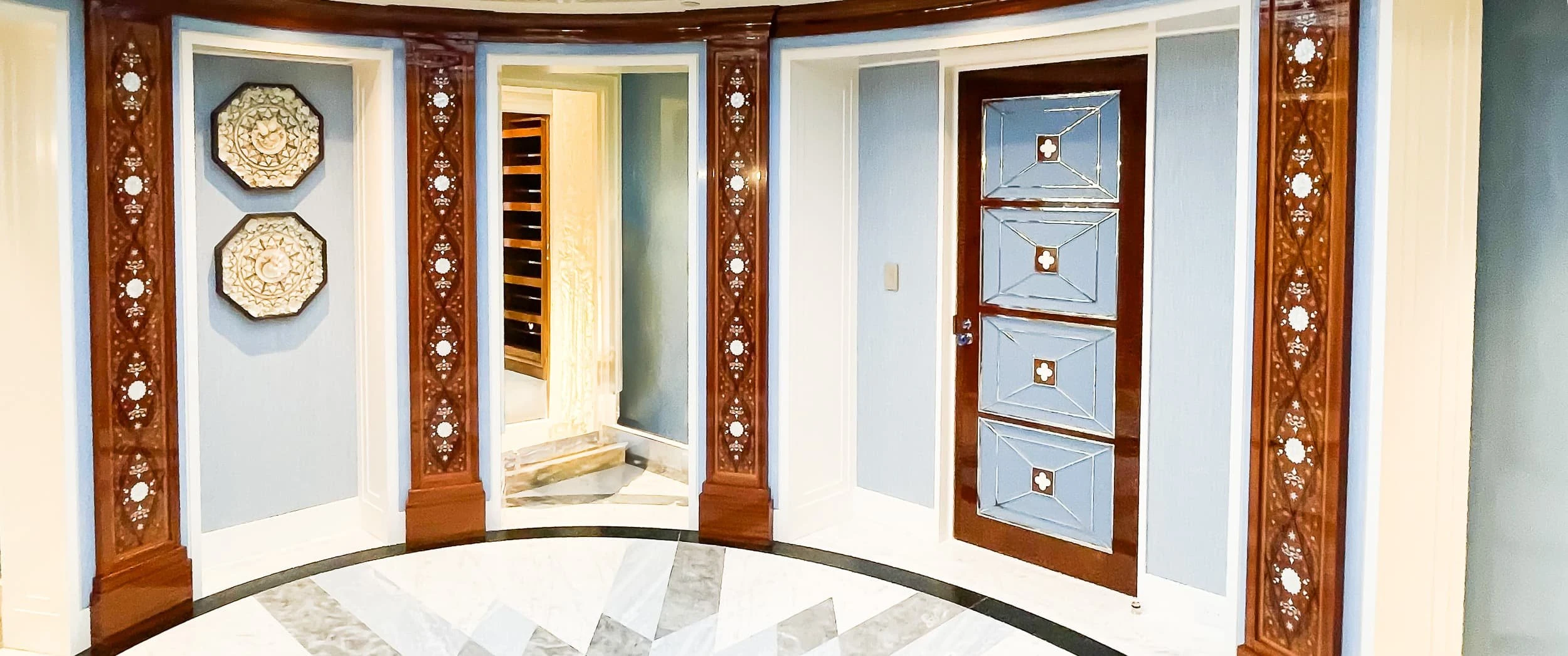 The finished curved lobby at the Rowes Wharf Apartment, with marquetry pilasters between pale blue panelled walls, a patterned marble floor and framed plates on the wall.