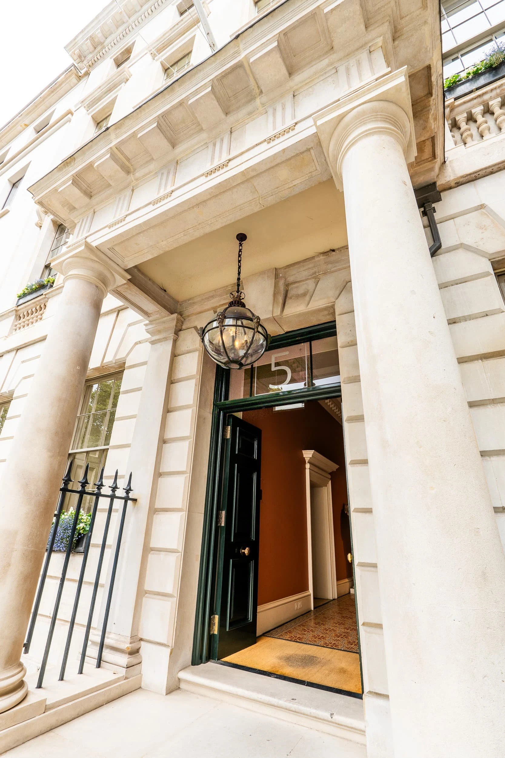 View up to the entrance portico at 5 St James's Square, with stone columns, traditional lantern and dark green door opening into a warm-toned lobby, hinting at the refined, residential quality of the private offices inside.