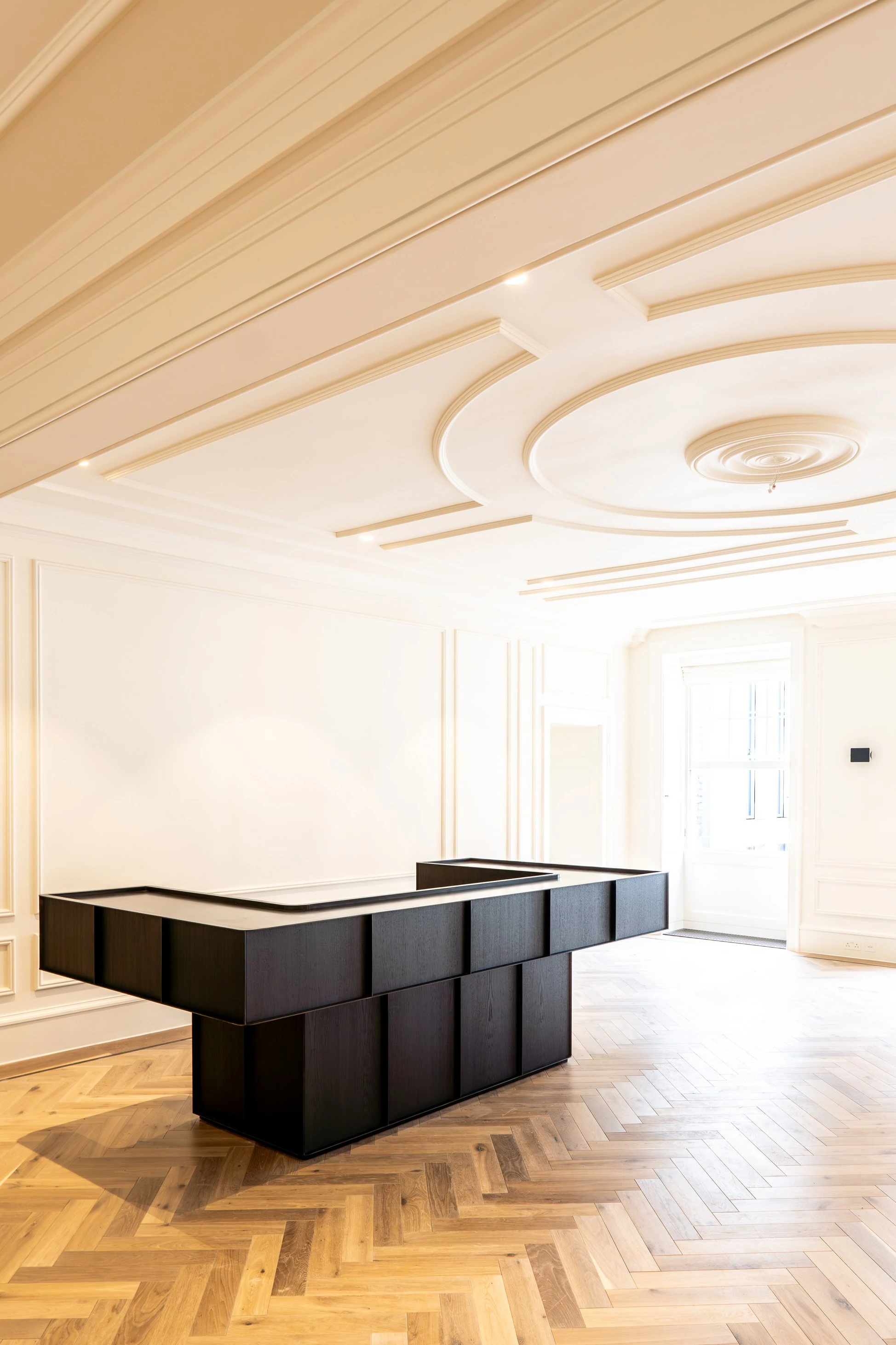 Finished reception area with the monumental graphite-stained oak and blackened steel desk set against classical panelling and herringbone flooring, creating a bold sculptural welcome for visitors.