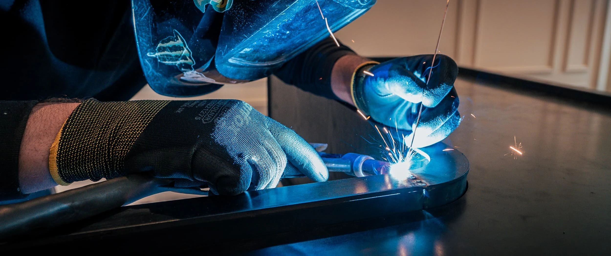 On-site welding of the curved steel sections of the reception desk, with sparks flying as fabricators join components that could not be brought in whole due to the building's tight access routes.