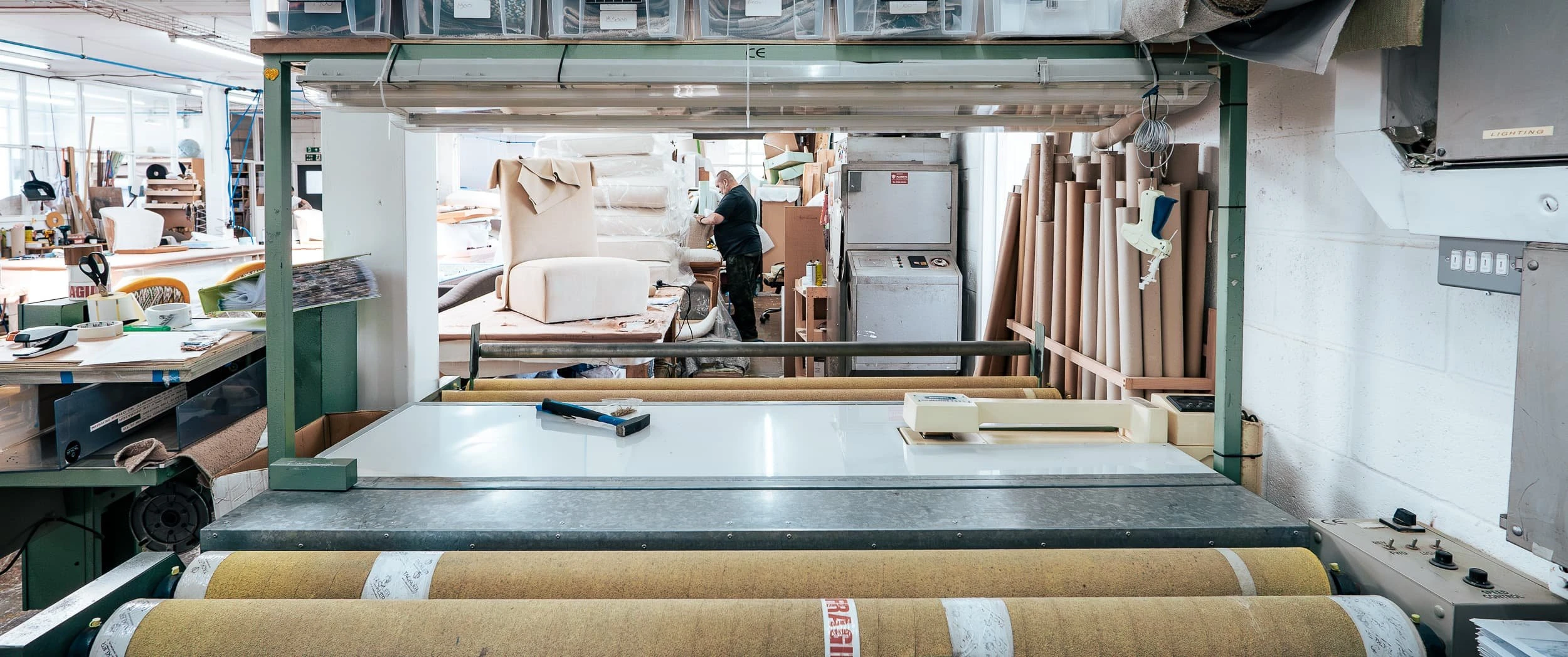 Wide shot of the upholstery workshop with rolls of fabric, benches and part-built chairs, illustrating the scale of bespoke production behind the soft seating for the St James's Square offices.