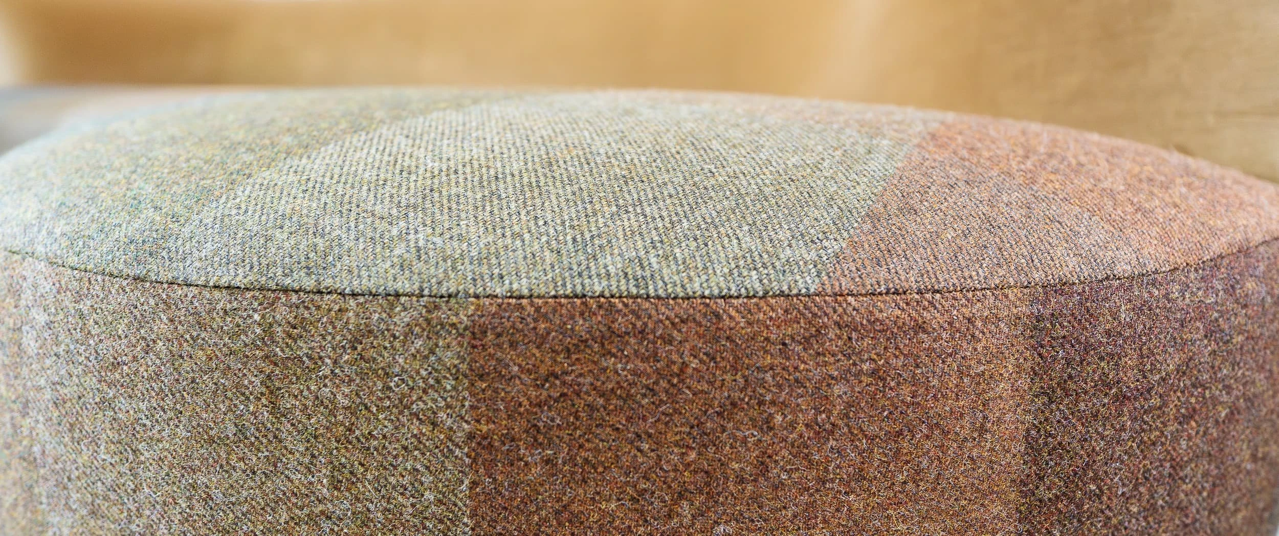 Close-up of a curved sofa seat upholstered in soft patchwork wool in earthy tones, showing the fine stitching, rounded profile and tailored bespoke upholstery used in the office lounge.