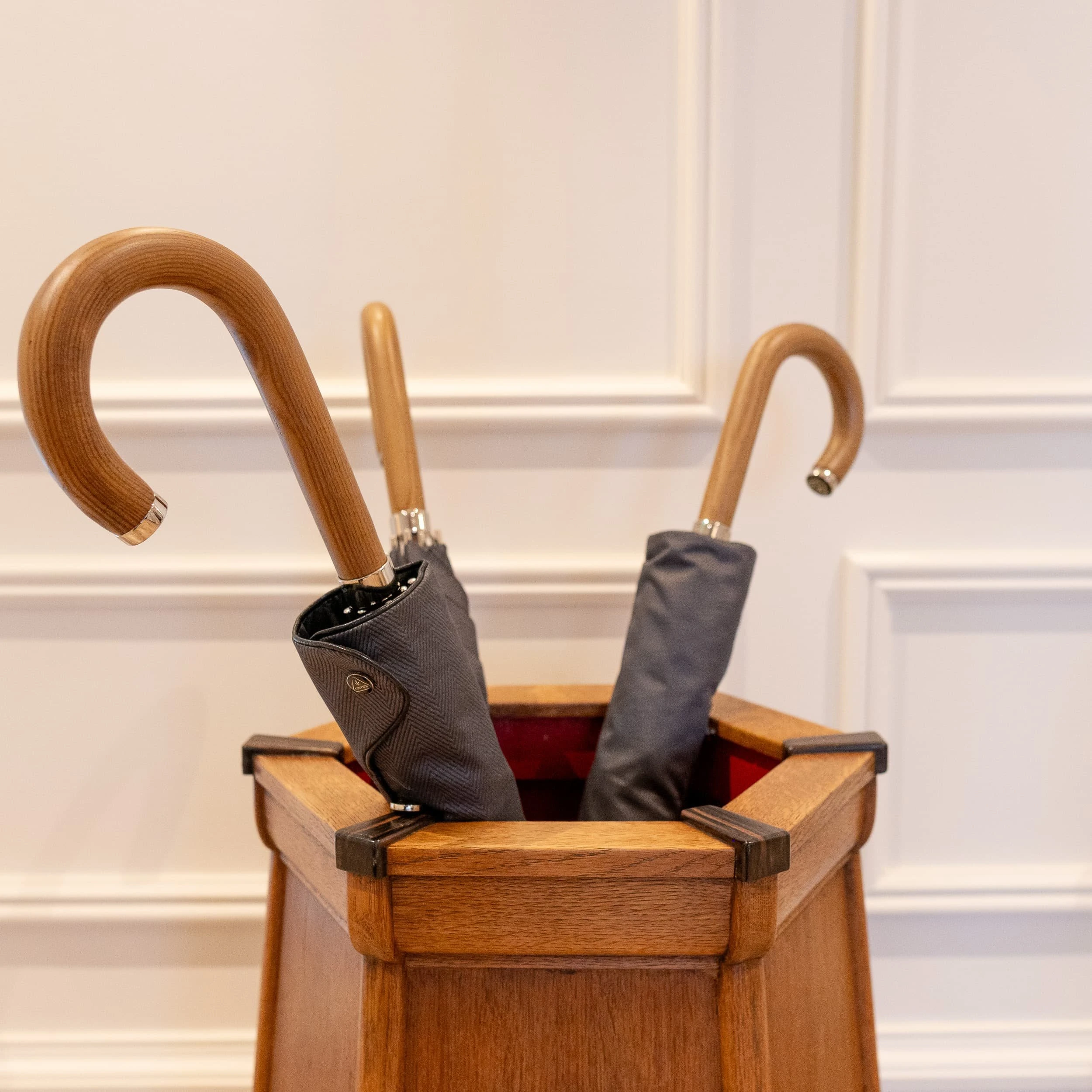 Detail shot of a traditional oak umbrella stand holding grey-handled umbrellas against crisp wall panelling, underscoring the genteel townhouse character of the St James's Square private offices.