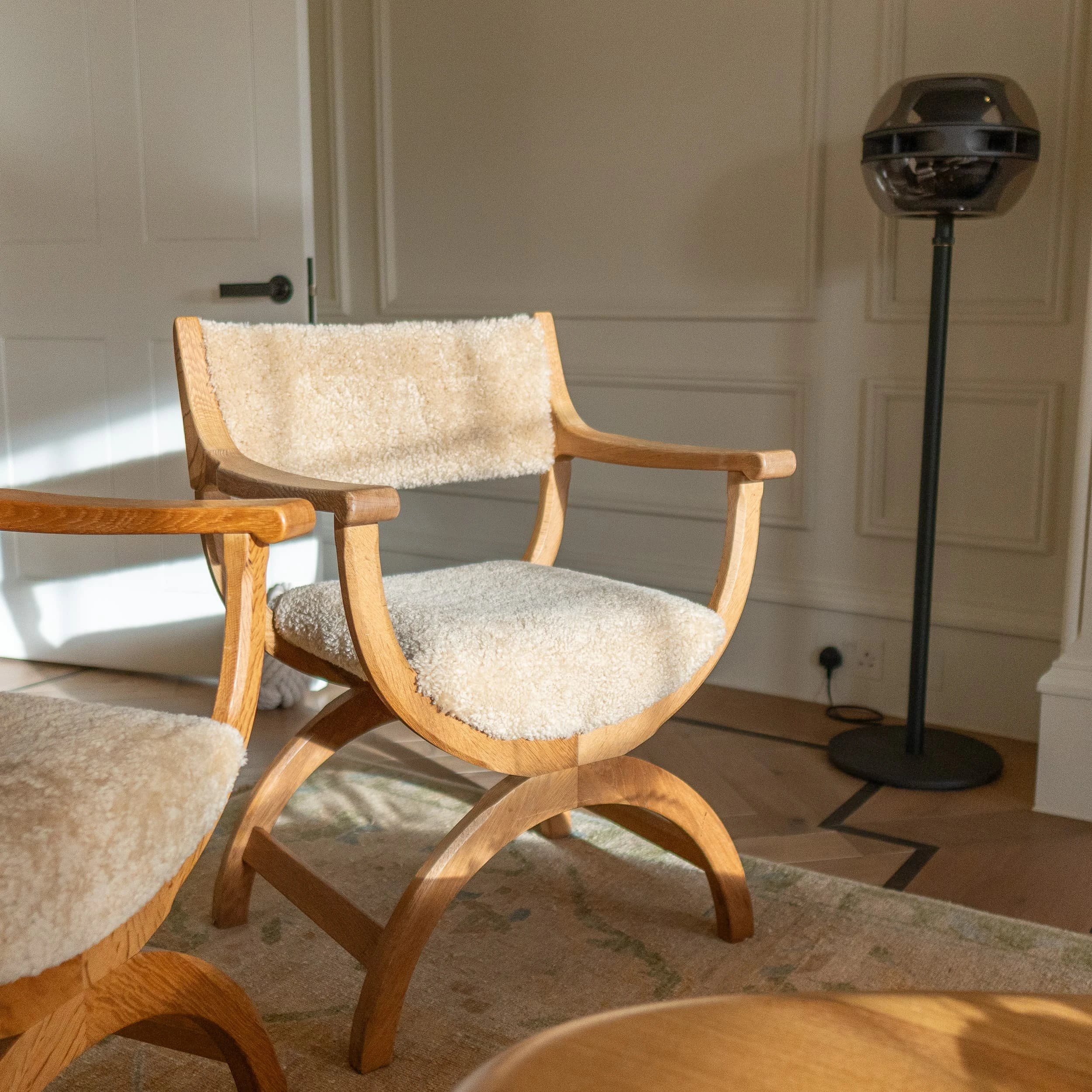 Close-up of a shearling-upholstered oak armchair beside a sculptural floor speaker in the lounge, the tactile boucle seat and backrest reinforcing the residential comfort of the office setting.