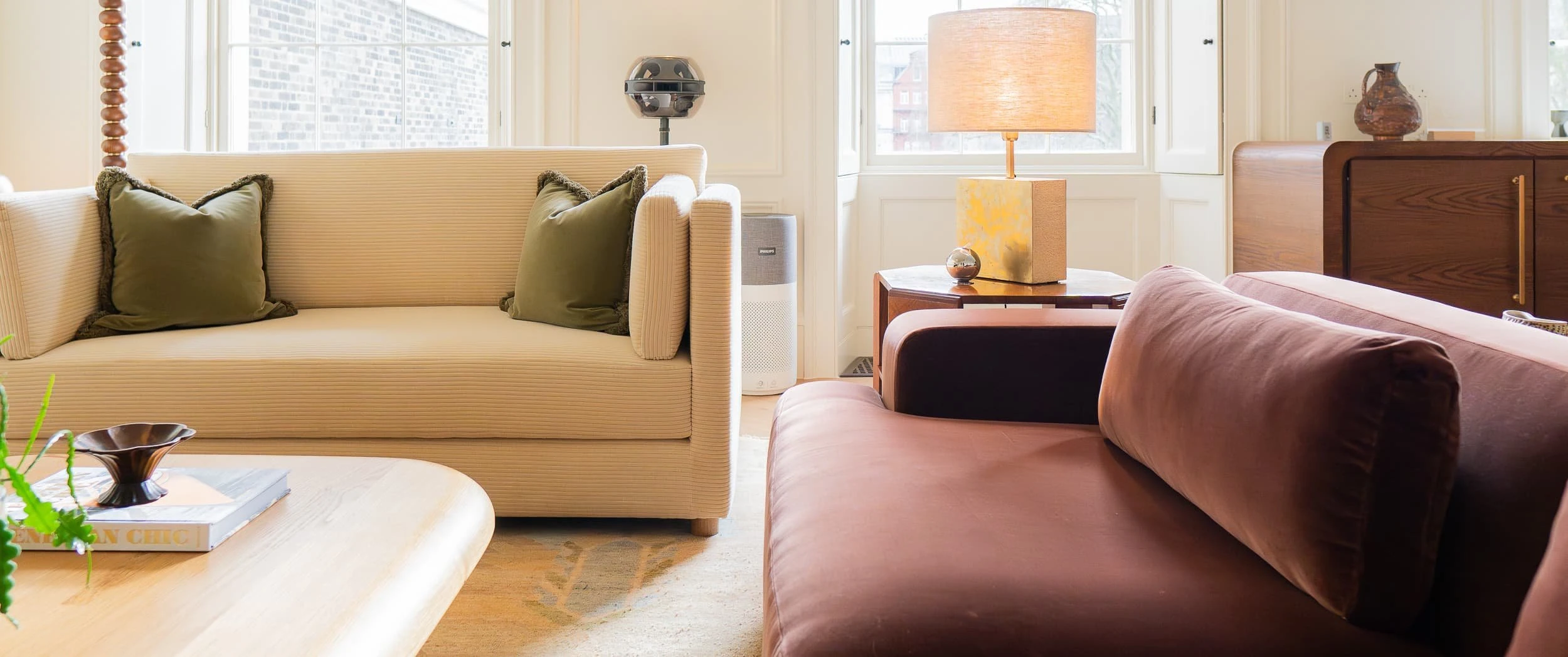 Detail of cream corduroy sofa and deep brown velvet sofa arranged around a timber coffee table, with table lamp and oak storage behind, highlighting the warmth and layered textures of the scheme.